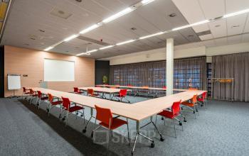 Vergaderruimte in kantoorpand Polarisavenue 1, Hoofddorp, met grote U-vormige vergaderopstelling, rode stoelen en tl-verlichting. De ruimte is klaar voor gebruik en geschikt voor kantoorruimte huren.