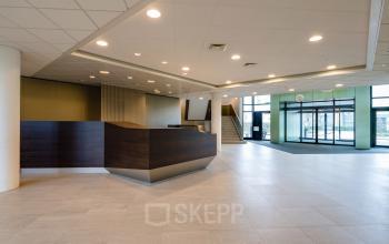 Lichte, ruime receptie in het kantoorpand Hoeksteen 54-72 in Hoofddorp met balie en toegang tot de trap en glazen deuren.