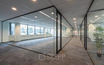 Ruime, lichte kantoorruimte huren in kantoorpand aan Hoeksteen 54-72 in Hoofddorp met glazen wanden en uitzicht op parkeerplaats.