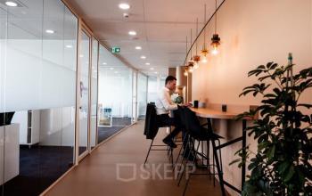 Moderne kantoorruimte in Hoofddorp op Mercuriusplein 1 met glazen wanden en een werkende persoon aan een hoge tafel. Geschikt voor creatieve en flexibele werkplekken.