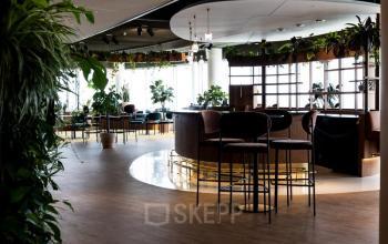 Een modern kantoorpand met een stijlvolle lounge op Mercuriusplein 1, Hoofddorp, gevuld met hoge stoelen en veel groen. Ideaal voor kantoorruimte huren.