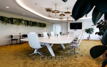 Moderne vergaderruimte met lange witte tafel en comfortabele stoelen, omgeven door groene accenten, in een kantoorpand op Mercuriusplein 1, Hoofddorp; ideaal voor kantoorruimte huren.