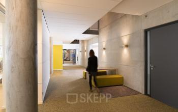 Modern kantoorpand aan de Opaallaan 1180 in Hoofddorp met strakke lijnen, zachte verlichting en een vrouwelijke professional. Ideale locatie om een kantoorruimte te huren voor zakelijke activiteiten.