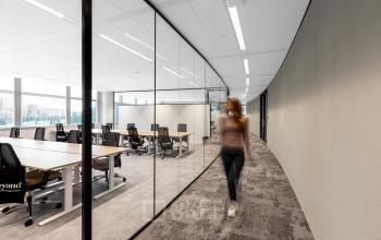 Moderne kantoorruimte met glazen wanden en bureaus op Taurusavenue 1-41 in Hoofddorp. Een persoon loopt langs de werkplekken.