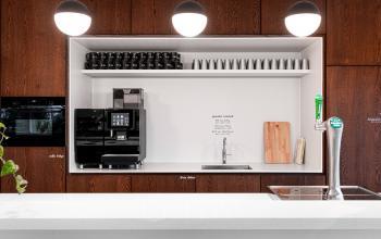 Een moderne pantry met een koffiezetapparaat, kraan, en glazen op een witte plank. Huur je kantoorruimte op Taurusavenue 1-41 in Hoofddorp.