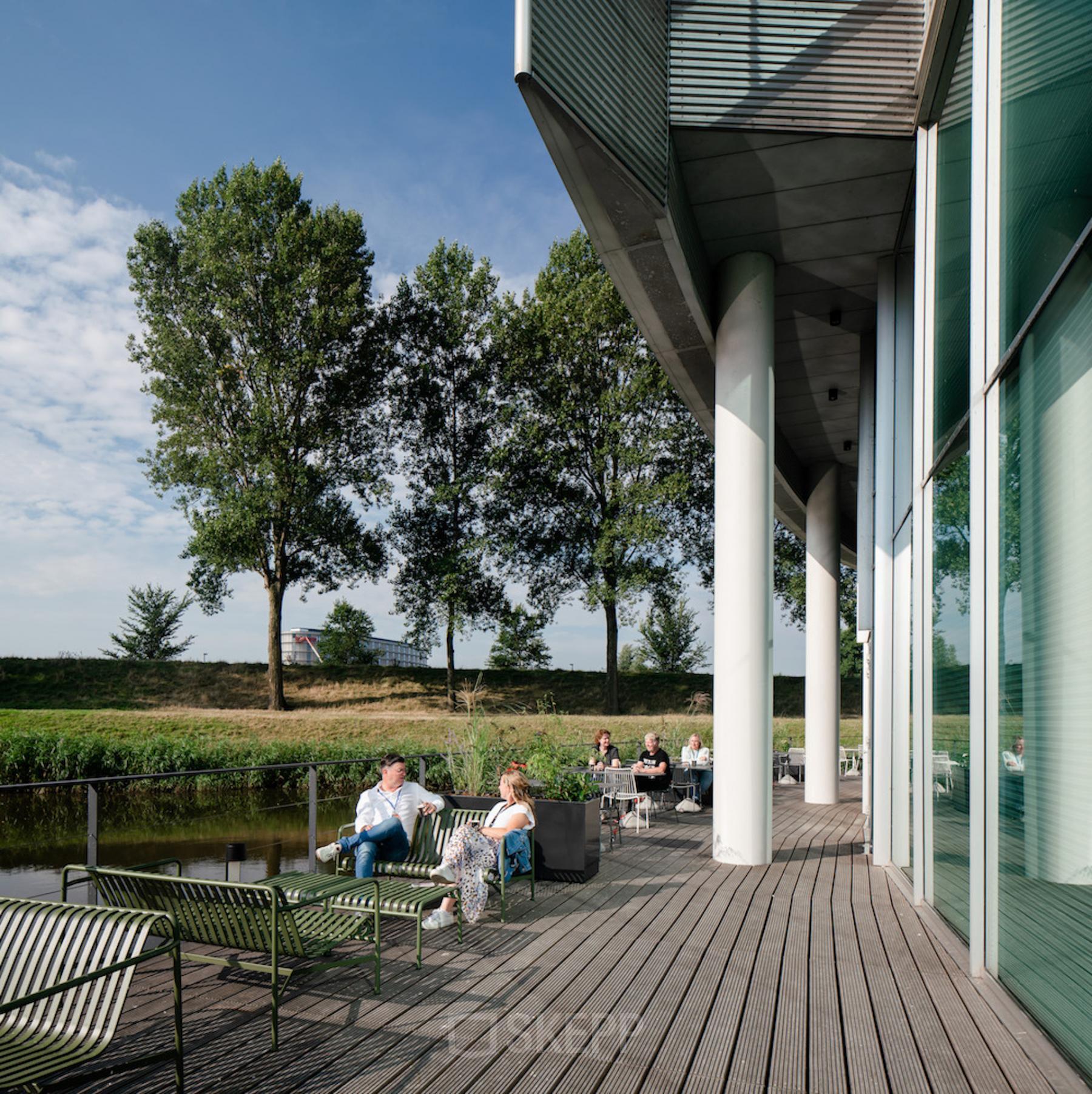 Kantoorruimte huren aan Taurusavenue 1-41 in Hoofddorp met een buitenruimte waar mensen ontspannen zitten aan tafels, omgeven door bomen en een waterkant.