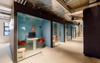 Moderne kantoorruimte op Siriusdreef 16 in Hoofddorp met glazen werkplekken, ideaal om kantoren te huren. Het interieur heeft glazen wanden en rode stoelen, wat een professionele uitstraling geeft.