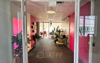 Informatieve en kleurrijke lobby van het kantoorpand aan Planetenweg 5, Hoofddorp. Mensen ontspannen en overleggen, in comfortabele stoelen omgeven door planten. Ideaal voor wie een kantoorruimte huren zoekt.