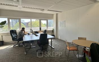 Een lichte kantoorruimte in Hoofddorp met bureaus en een vergadertafel, waar een persoon achter een computer werkt. Ideaal voor bedrijven die kantoorruimte willen huren.