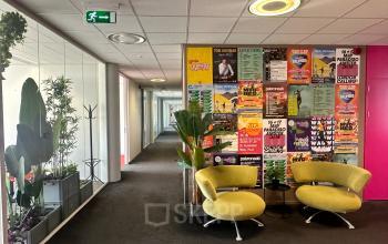 Lounge ruimte met kleurrijke stoelen en een muur vol concertposters in het kantoorpand op Planetenweg 5, Hoofddorp.