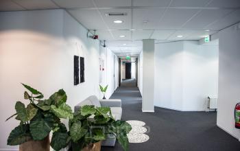 Een lichte gang in een kantoorpand op Meidoornkade 19, Houten, met planten, een fauteuil en voldoende verlichting. Ideaal voor wie kantoorruimte wil huren.