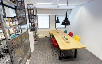 Gezellige vergaderruimte in Houten met kleurrijke stoelen en een lange houten tafel, ideaal voor een bijeenkomst in het kantoorpand aan de Meidoornkade 22.