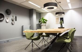 Vergaderruimte in Houten met grote houten tafel en groene stoelen, geschikt voor kantoorruimte huren.