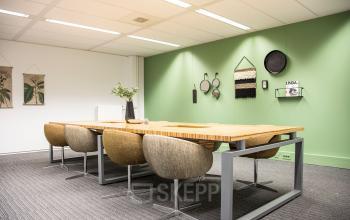 Moderne vergaderruimte in kantoorpand op Meidoornkade 22, Houten met lange houten tafel en comfortabele stoelen, tegen een groene wand met decoraties. Ideaal voor kantoorruimte huren.