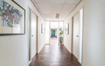 Heldere gang in een kantoorpand op Sandtlaan 36, Katwijk, met houten vloer en kunst aan de muur. Ideaal voor bedrijven die kantoorruimte willen huren met ruimte voor creativiteit en productiviteit.