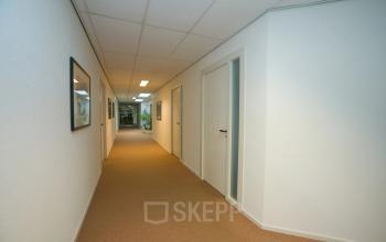 Verlichte gang met bruin tapijt en witte muren in kantoorpand op Sandtlaan 36, Katwijk. Verschillende deuren zichtbaar. Kantoorruimte huren mogelijk.