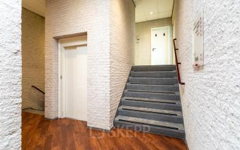 Entree van een kantoorpand op Sandtlaan 36 in Katwijk met witte bakstenen muren en een trap naar boven. Ideaal voor bedrijven die kantoorruimte willen huren.