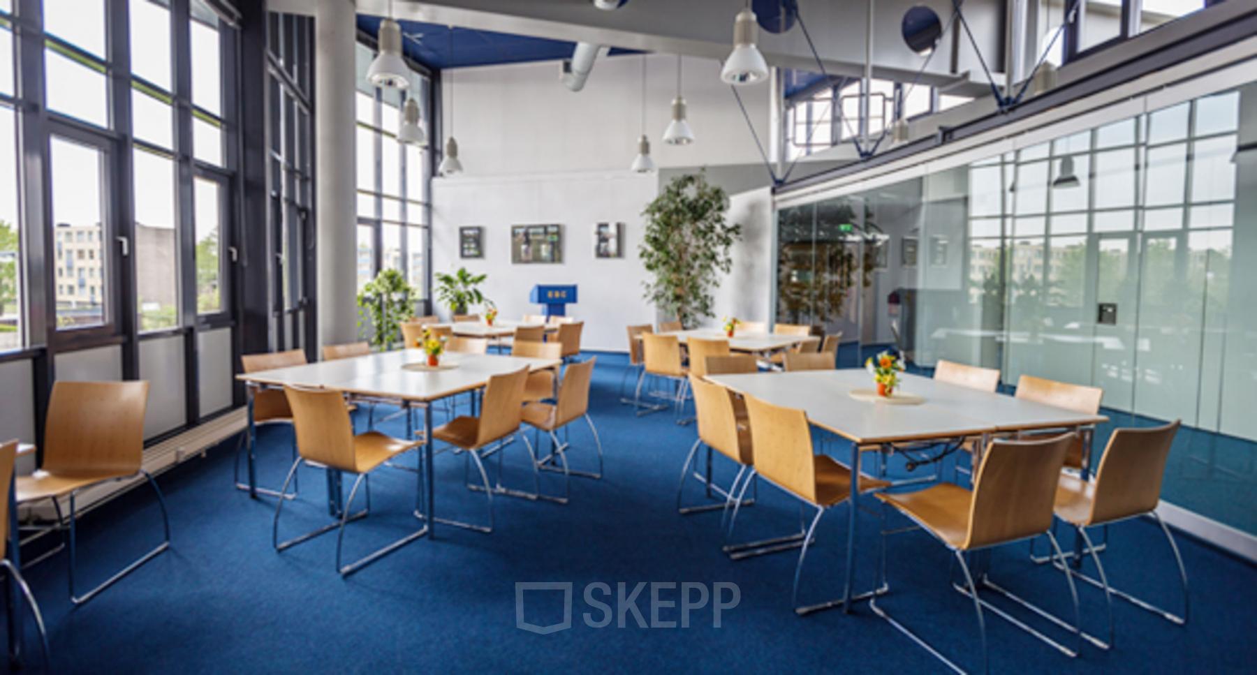 Lichte, moderne kantoorruimte met blauwe vloerbedekking, houten stoelen en witte tafels, ideaal voor vergaderingen bij kantoorpand Eurodepark 1 in Kerkrade.