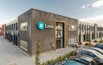 Exterieur van het kantoorpand op Industriepark 5B in Leek, Leek, met moderne gevel en geparkeerde auto's. Perfecte locatie om een kantoorruimte te huren voor zakelijke activiteiten.