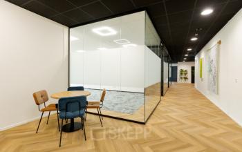 Moderne kantoorpand interieur in Leek met glazen wanden en houten vloer, ideaal voor kantoorruimte huren. Stijlvolle en functionele inrichting met vergadertafels en comfortabele stoelen.