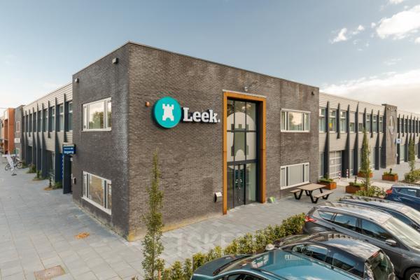 Exterieur van het kantoorpand op Industriepark 5B in Leek, Leek, met moderne gevel en geparkeerde auto's. Perfecte locatie om een kantoorruimte te huren voor zakelijke activiteiten.