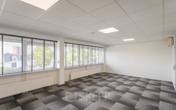 Lichte kantoorruimte te huur op Ouddeelstraat 7a, Leeuwarden, met grijze vloerbedekking en grote ramen met uitzicht. Een veelzijdige ruimte voor diverse zakelijke activiteiten.