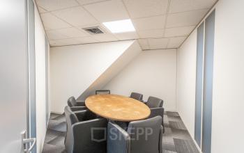 Vergaderruimte met ovale houten tafel en zes grijze stoelen in het kantoorpand op Ouddeelstraat 7a, Leeuwarden, ideaal voor kantoorruimte huren.