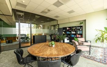 Gezellige kantoorkamer in kantoorpand op Lange Marktstraat 1 in Leeuwarden met ronde houten tafel, stoelen, en planten. Heldere werkruimte met glazen vergaderruimte op de achtergrond.