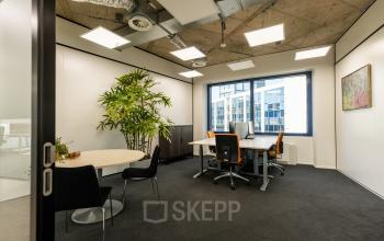 Kantoorruimte huren op Lange Marktstraat 1, Leeuwarden. Licht kantoor met tafels, stoelen en een grote plant nabij het raam.