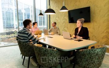 Moderne vergaderruimte met grote tafel, ergonomische stoelen en hanglampen, in gebruik door enkele mensen voor zakelijke besprekingen, gelegen in kantoorpand op Lange Marktstraat 1, Leeuwarden.