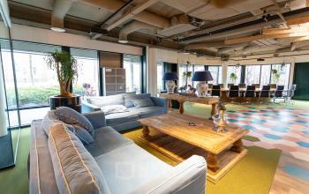 Ruime werkplek in kantoorpand aan Schipholweg 103, Leiden, met comfortabele zithoek, lange vergadertafel, veel natuurlijk licht en moderne inrichting.