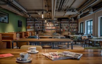 Gemeubileerde werkruimte met lange tafels en stoelen, boekenplanken langs de muur en diverse gebruiksartikelen op de tafels bij kantoorruimte Schipholweg 103, Leiden.