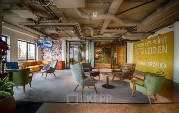 Gezellige en moderne lounge in kantoorpand gelegen aan Schipholweg 103 in Leiden, met diverse zitmogelijkheden en kleurrijke accenten. Ideaal voor informeel overleg of ontspannen pauze tijdens kantooruren.