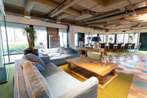 Ruime werkplek in kantoorpand aan Schipholweg 103, Leiden, met comfortabele zithoek, lange vergadertafel, veel natuurlijk licht en moderne inrichting.
