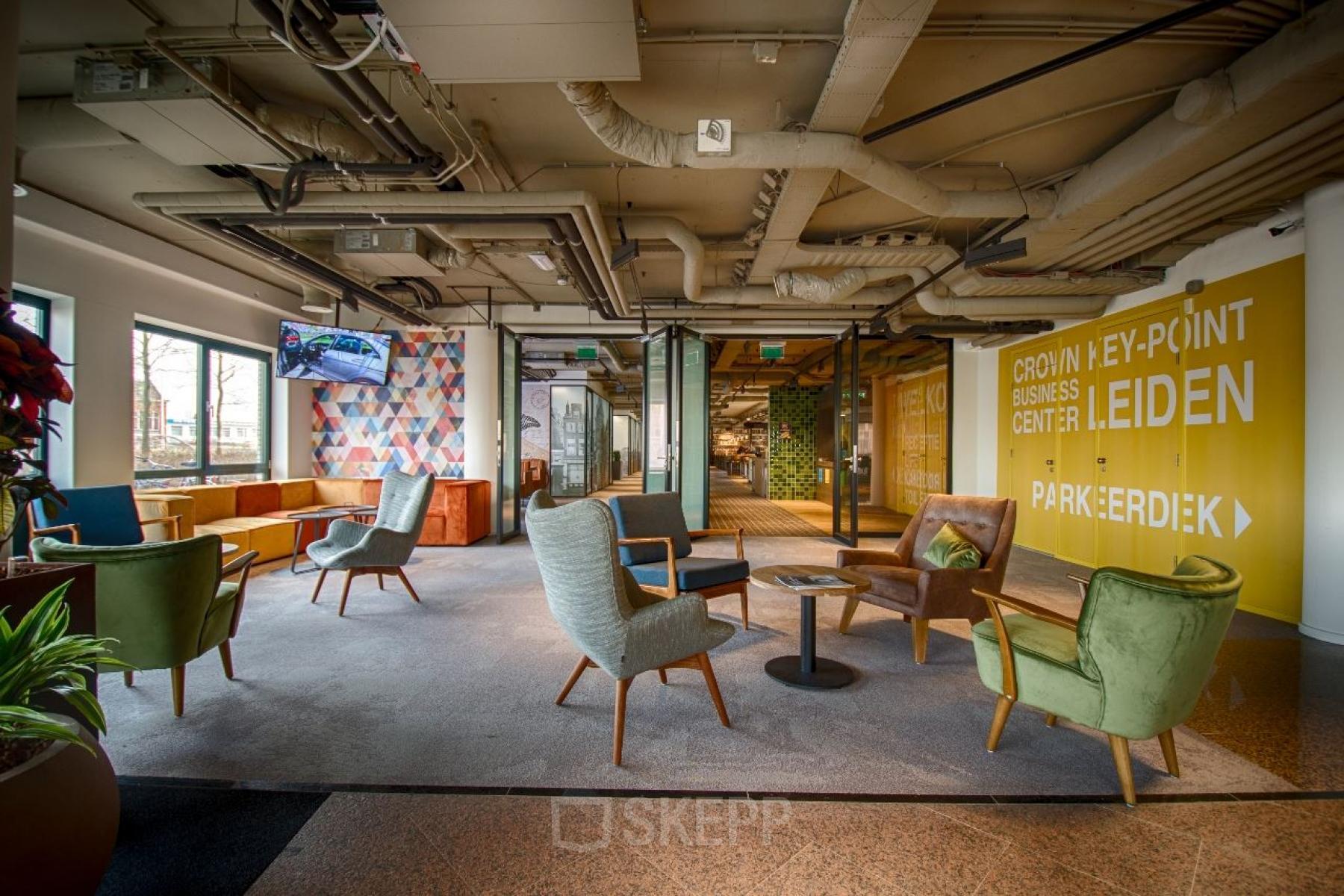 Gezellige en moderne lounge in kantoorpand gelegen aan Schipholweg 103 in Leiden, met diverse zitmogelijkheden en kleurrijke accenten. Ideaal voor informeel overleg of ontspannen pauze tijdens kantooruren.