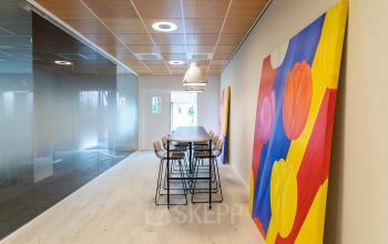 Modern kantoorpand op Pompoenweg 3 - 15 in Leiden met kleurrijke kunst, hoge stoelen en glazen wanden.