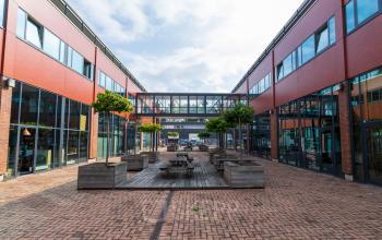 Kantoorpand op Pompoenweg 3-15 in Leiden met buitenruimte tussen gebouwen voorzien van houten tafels en plantenbakken.