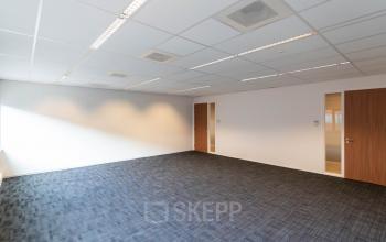 Leeg kantoorpand aan de Pompoenweg 3 - 15, Leiden, met donkere vloerbedekking, witte muren, twee houten deuren, en systeemplafond met TL-verlichting.
