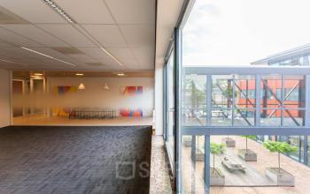 Kantoorruimte huren in Leiden op Pompoenweg 3 - 15, met grote ramen die uitzicht bieden op een binnenplaats. Het interieur bevat een vergaderruimte met kleurrijke achtergrond en een tapijtvloer.