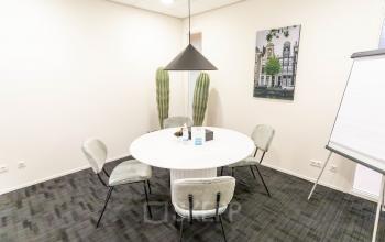 Een lichte vergaderruimte in een kantoorpand op Pompoenweg 3 - 15, Leiden, met een ronde tafel, vier stoelen en een flipover, ideaal voor kantoorruimte huren.