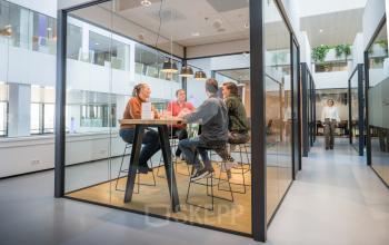 Kantoorruimte huren op Bargelaan 200 in Leiden met moderne inrichting en glazen wanden. Mensen in vergaderruimte aan een hoge tafel in gesprek.
