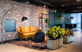 Moderne lounge in het kantoorpand aan Bargelaan 200, Leiden met een gele bank, zwarte fauteuil en planten. Kantoorruimte huren in dit pand mogelijk.