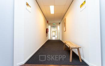 Heldere gang in het kantoorpand aan de Fruitweg 22 in Leiden, met witte muren en een houten bank langs de zijkant.