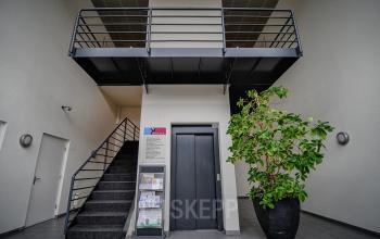 Entree van het kantoorpand op Fruitweg 22 in Leiden met een lift, trap en grote plant. Ideaal voor wie kantoorruimte wil huren.