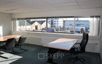 Kantoorruimte huren op Fruitweg 22 in Leiden met grote ramen, veel daglicht, enkele bureaus en stoelen, ideaal voor zakelijke activiteiten.