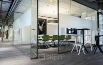 Vergaderruimte in kantoorpand Kanaalpark 140, Leiden met glazen wanden, groene stoelen en vergadertafel omringd door moderne inrichting.