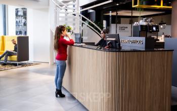 Modern kantoorpand met receptie en ontvangstbalie op Kanaalpark 140, Leiden. Twee mensen zijn in gesprek terwijl een derde persoon zit in een loungehoek op de achtergrond.