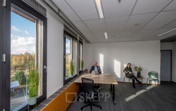 Kantoorruimte huren aan de Fokkerstraat 16 in Leusden met grote ramen, planten en personen bezig met laptops in een moderne werkomgeving.
