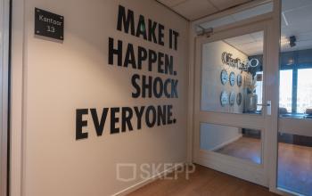 Lichte entree van kantoorpand aan Horsterweg 24, Maastricht-Airport, met opvallende muurtekst en glazen deur. Ideaal voor bedrijven die kantoorruimte willen huren in een moderne omgeving.