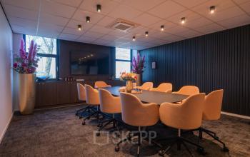 Vergaderruimte in kantoorpand op Horsterweg 24, Maastricht-Airport met ovale tafel en comfortabele stoelen, geschikt voor zakelijke bijeenkomsten. Moderne verlichting en decoratieve bloemen. Optimaal voor kantoorruimte huren.